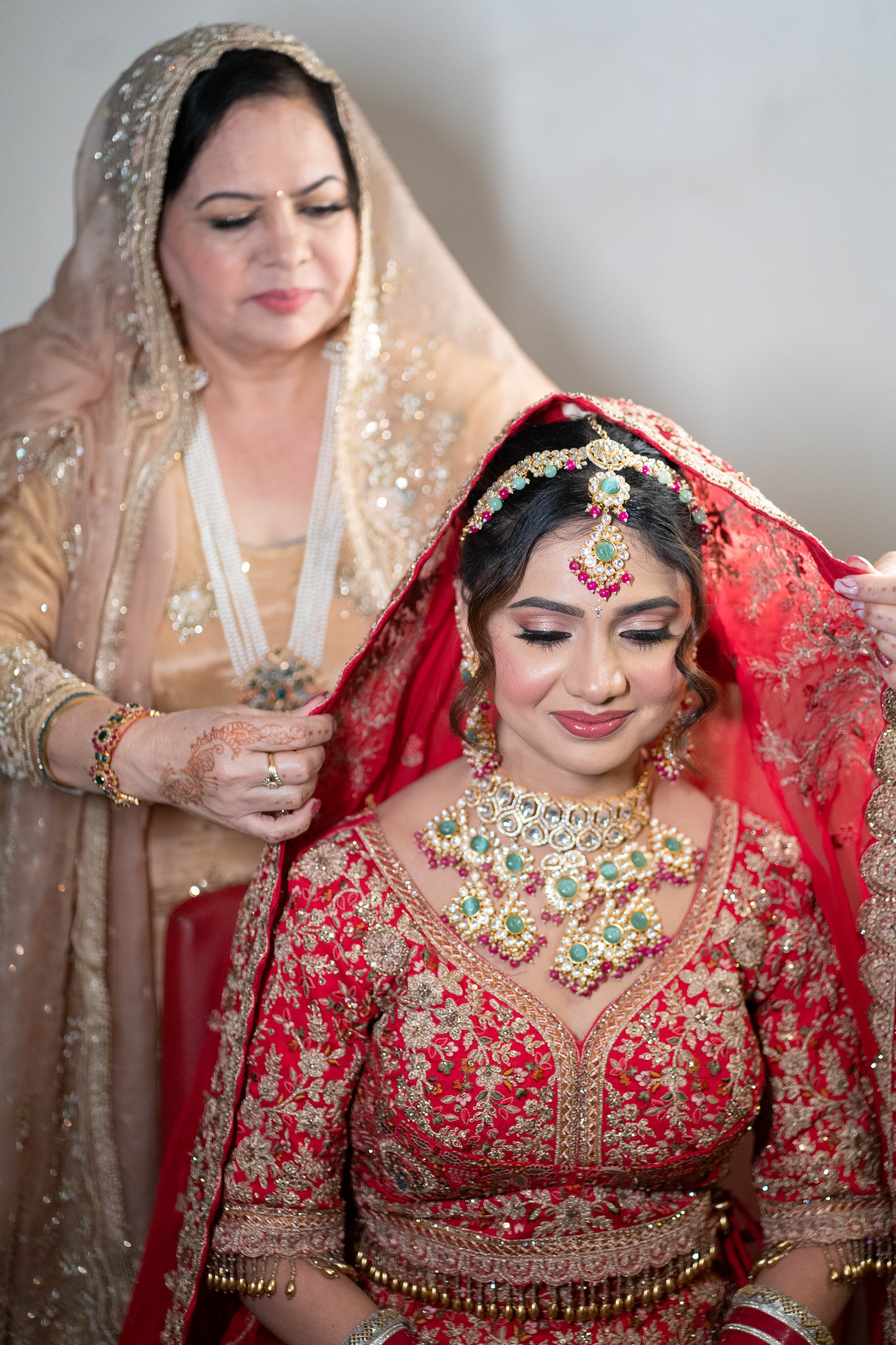 Mother helping bride with traditional red veil